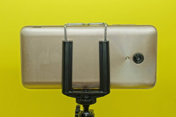 one brown smartphone in a black tripod mount on a yellow background