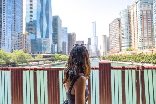Woman walking on a bridge going over a green river in the middle of a city