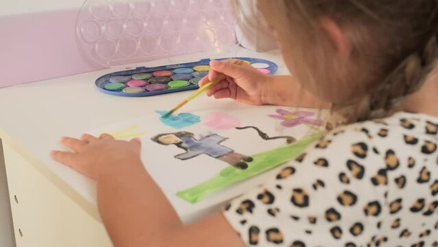 Talented Creative Child Girl Female Artist Draws with Her Hands on Paper, Using Fingers Paints Brush Creates Colorful, Kid Drawing on table at Home. Painter Creating Abstract Modern Art. Childhood