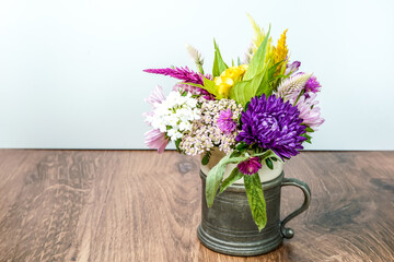 A beautiful bouquet of flowers in a tavern mug. Placed on a wood table with a white background. 