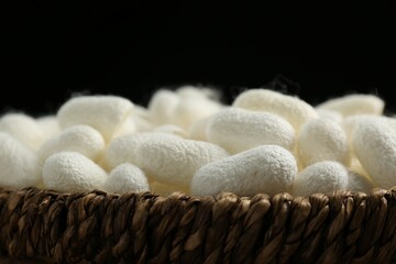 White silk cocoons in wicker bowl on black background, closeup