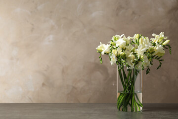 Beautiful freesia flowers in vase on grey table. Space for text
