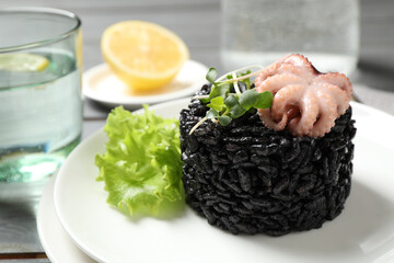 Delicious black risotto with baby octopus on table, closeup