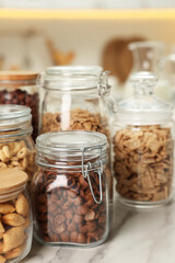 Glass containers with different breakfast cereals on white marble table in kitchen