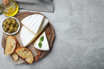 Tasty brie cheese with olives, basil, bread and almonds on grey table, flat lay. Space for text