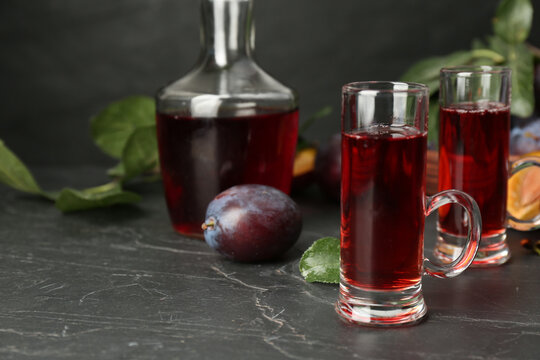 Delicious plum liquor and ripe fruits on black table. Homemade strong alcoholic beverage