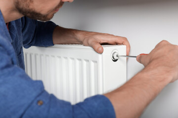 Man with screwdriver fixing radiator at home, closeup