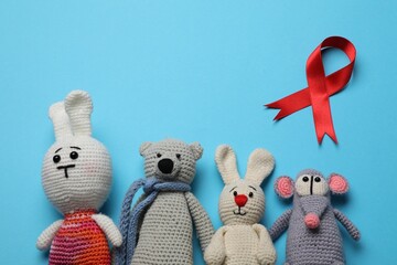 Cute knitted toys and red ribbon on blue background, flat lay. AIDS disease awareness