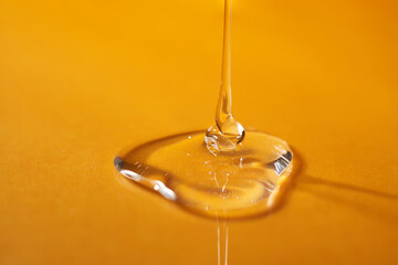 A drop of body gel or shampoo pouring from above on a yellow saturated background.