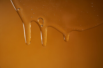 A drop of body gel or shampoo flowing down on a yellow saturated background. Texture.