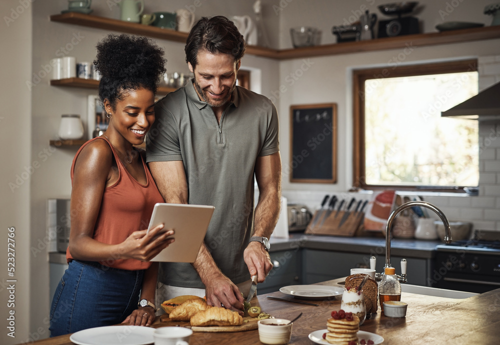 Canvas Prints Young couple cooking healthy food together following recipes online on a tablet, step by step. Happy, cheerful and smiling husband and wife making dinner in the kitchen at home.