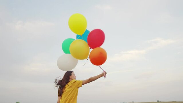 young girl with air beautiful balloons against blue sky. walk child nature. festive mood teenager. happy carefree. hold gel balls hand. blue green red orange yellow colors. fun one person journey.