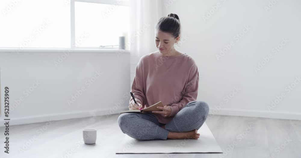 Poster Young woman writing candid notes in a journal while sitting on a floor at home. Relaxed, carefree female daydreaming, listing her goal, vision or plan in a diary and enjoying free time on a weekend