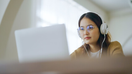 Young asian woman wearing glasses and headset working on computer laptop at house. Work at home,...