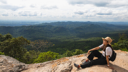 Asian woman travel and sitting on the edge of the mountain with forest landscape background.Concept of travel in spring season at Thailand.