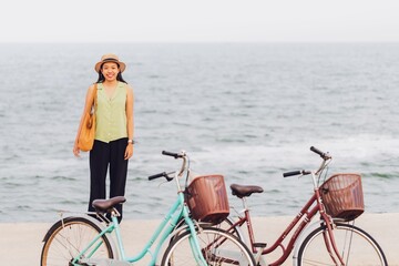 Fototapeta na wymiar Asian traveler woman traveling with bicycle at beach by the sea background.Concept of a happy summer holiday travel.