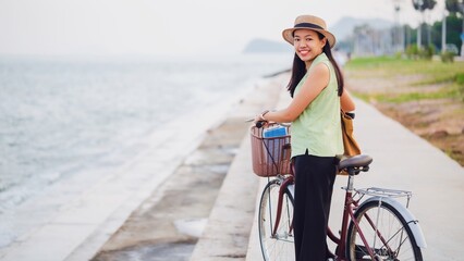 Obraz na płótnie Canvas Asian traveler woman traveling with bicycle at beach by the sea background.Concept of a happy summer holiday travel.