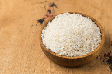Raw round white rice in a wooden bowl on a wood background. Copy space