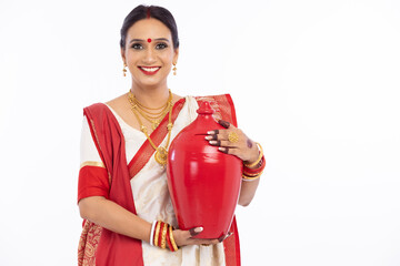 Portrait of beautiful bengali woman holding earthen piggy bank in traditional red and white sari 
