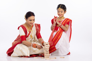 Happy bengali mother with daughter playing jenga together in traditional clothing
 - obrazy, fototapety, plakaty