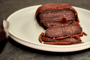 sliced basturma on a plate next to a bottle of wine and a glass