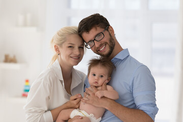 Portrait of loving parents and newborn look at camera. Happy young family with infant baby pose for...
