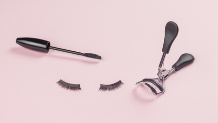 Eyelash curlers, brush and false eyelashes on a pink background.
