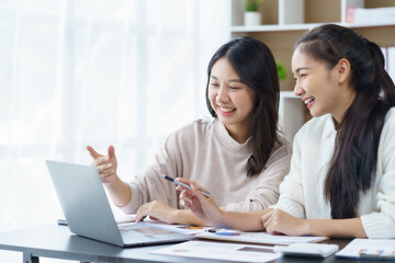 Two beautiful Asian businesswomen working together using laptop computer work together consult and advise on working together to plan work in new product.