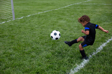 Young African American soccer player kicking the ball into the goal during a soccer game on a large grass field