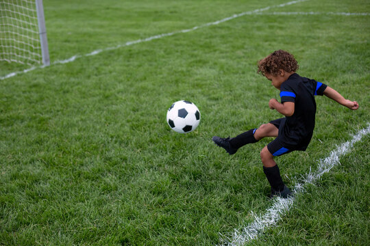 Young African American soccer player kicking the ball into the goal during a soccer game on a large grass field