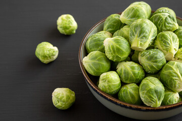 Raw Organic Brussel Sprouts in a Bowl on a black background, side view.