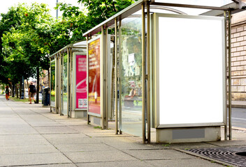 Fototapeta premium bus shelter at tram and bus stop. image collage. white poster ad display. advertising concept. glass and steel design. blurred color posters. urban setting with green trees in the background