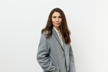 vertical portrait of a beautiful, sweet woman in a warm, stylish, autumn coat smiling pleasantly at the camera while standing against a light background