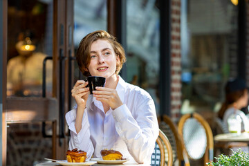Caucasian woman sipping a hot espresso coffee while sitting outside the european style cafe bistro enjoying slow life with morning vibe at the city square with sweet pastry