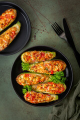 Dinner with oven baked Zucchini stuffed with chicken meat, belle peppers, tomatoes and cheese on a dark green table surface. Directly Above, vertical image.