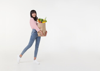 Beautiful smiling Asian woman holding shopping bag full of groceries and looking to copy space aside isolated on white background.