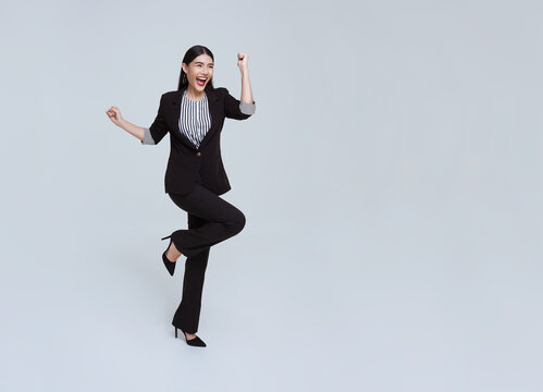 Happy cheerful young Asian businesswoman in suit jumping in mid-air isolated on studio white background.
