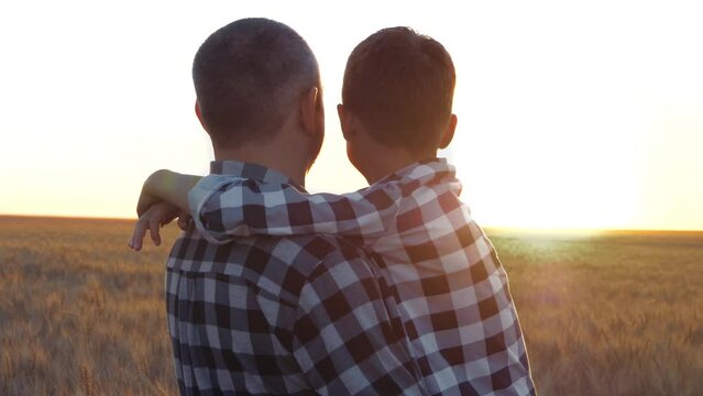 Dad holds his son in his arms. A family looks at the sunset in a wheat field. The concept of a happy family, grain export and import, agriculture. A happy child hugs his father.