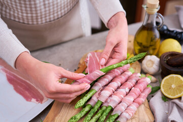 woman cooking green aspargus covered with bacon at domestic kitchen