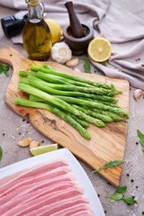 Green organic natural Asparagus on wooden cutting board and slice bacon at kitchen table