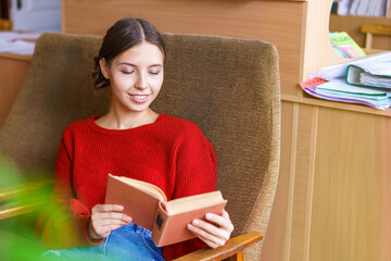 Cheerful brunette young woman laughing at funny story from book, happy with free time in office with collection of literature, positive young hipster girl enjoy relaxing with interesting novel
