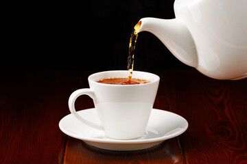 Tea is poured from the teapot into a cup. Porcelain teaware. Side view. Selective focus.