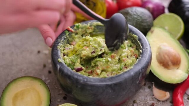 Making guacamole sauce - woman mixing chopped ingredients in marble bowl mortar
