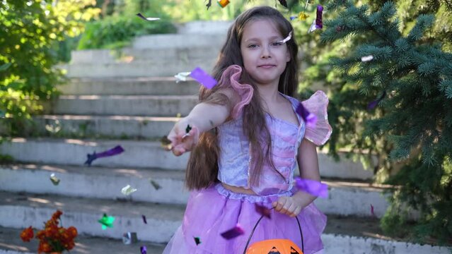 A little white girl, in a purple witch costume, throws colorful candy wrappers from a pumpkin flashlight into the camera. Happy Halloween meeting.