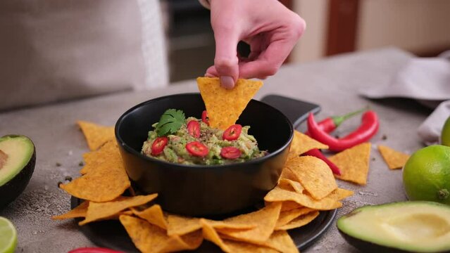 woman dips nachos chips to freshly made guacamole dip sauce in marble bowl mortar