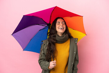 Young woman holding an umbrella isolated on pink background laughing