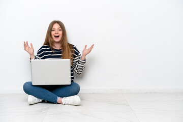 Young caucasian woman with a laptop sitting on the floor isolated on white background with surprise facial expression