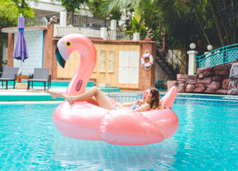 Happy smile young adult asian woman float on flamingo inflatable at hotel swimming pool