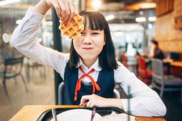  Happy young asian woman in japanese uniform student at cafe with waffle
