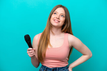 Singer caucasian woman picking up a microphone isolated on blue background thinking an idea while looking up
